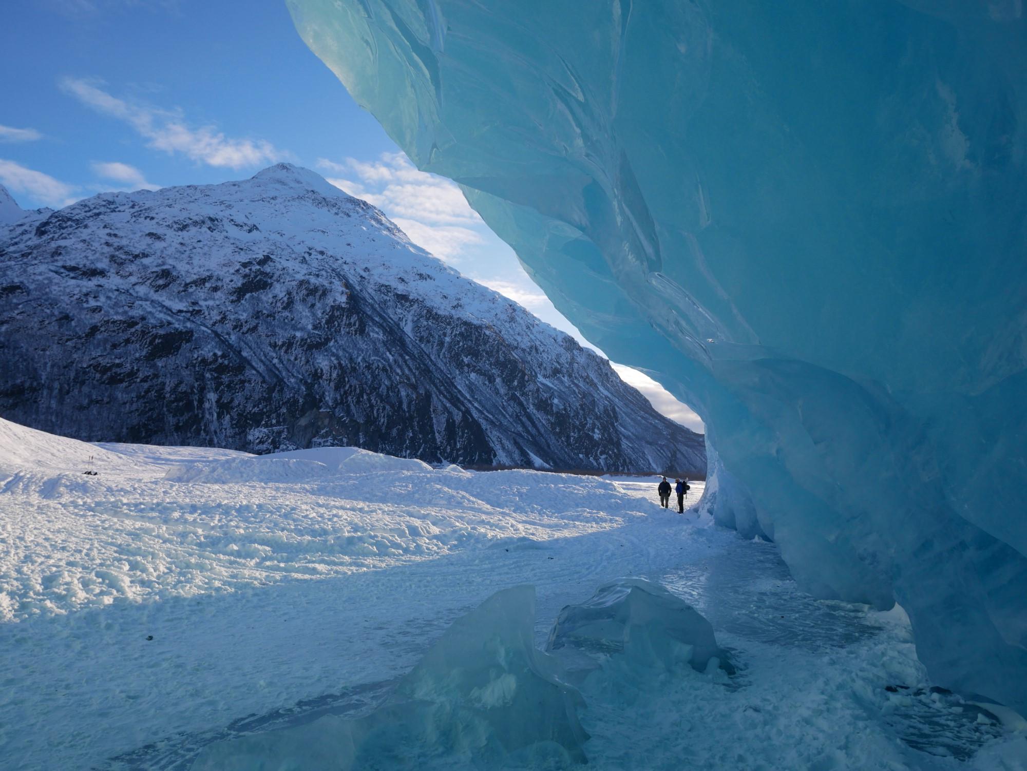 two people standing in between a snowy mountain and a large scale of ice